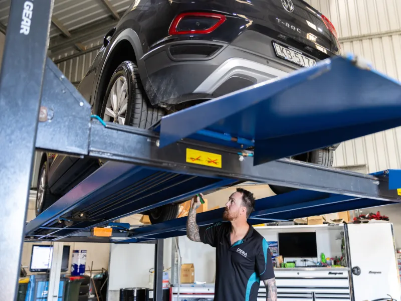 Dylan mechanic looking with torch underneath car on the hoist for a service